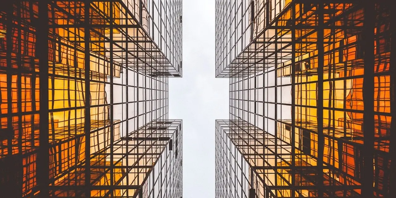 An architectural photograph looking skywards between two highly reflective buildings